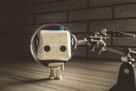 wooden robot android stands on a table under a magnifying glass. metal clamps with a magnifying glass. the face of a robot in the beautifying glass. AI study conceptの写真素材