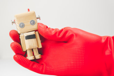 a hand in a red rubber glove grabs a small toy wooden robot. concept of zero-waste productionの写真素材