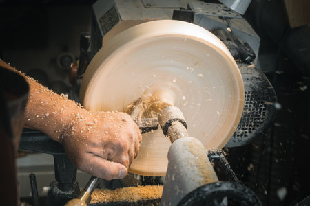 a man in a working apron works on a wood turning lathe. hands hold a chisel. hobby