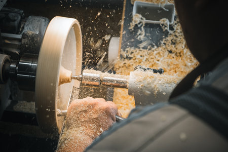 a man in a working apron works on a wood turning lathe. hands hold a chisel. hobbyの写真素材