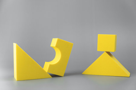 group of volumetric yellow geometric shapes on a gray background. simple shapes. cube on the edge of a triangleの写真素材