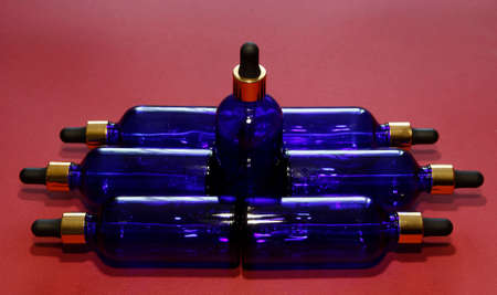 Sorted blue glass bottles with a golden dropper on a red