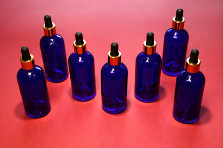 Sorted blue glass bottles with a golden dropper on a red