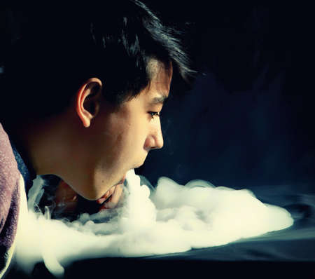 Vape trick waterfall in performance of vaper on dark background at overexposureの写真素材
