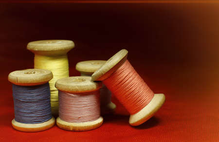 Old wooden coils of thread on an orange red fabric on a black background close upの写真素材
