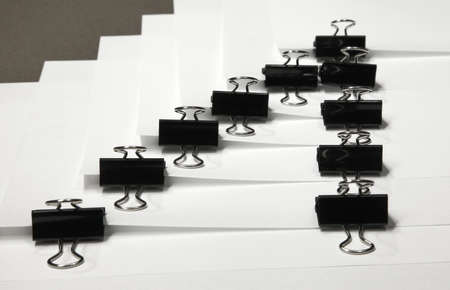Black binder clips in a row clamping the paper close up white background