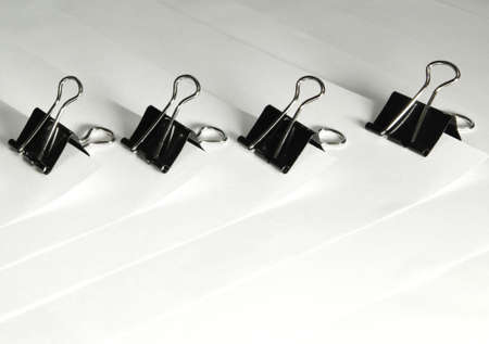 Black binder clips in a row clamping the paper close up white backgroundの写真素材