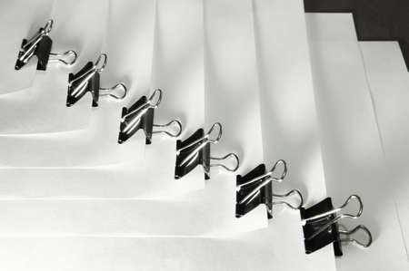 Black binder clips in a row clamping the paper close up white backgroundの写真素材