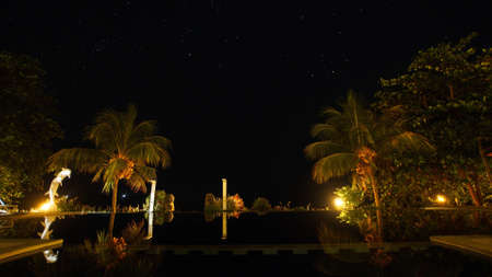 Luxury hotel with a swimming pool and palm trees under the starry sky. Time-lapse, long exposure,...