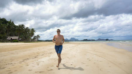 Man running along beach. Fitness sports runner man jogging on beach. Handsome young fit sporty male athlete running outside on beautiful beach training.の写真素材
