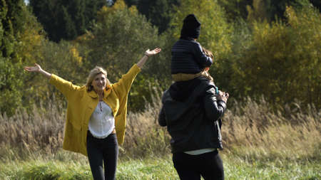 Happy mother, father and little son walking in autumn park and having fun.Son sits on his fathers...