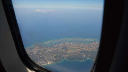 View through an airplane window on the tropical island, ocean, sky and clouds. Aerial view sea, clouds and sky as seen through window of an aircraft. Travel concept.の写真素材