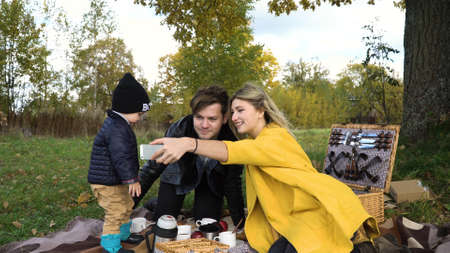 Smiling family taking selfie sitting on the grass in a city park. Young family with son at a picnic in the park on a sunny day.Family having picnic outdoors.の写真素材