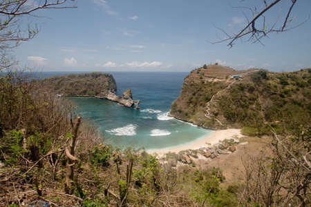 Beach with with azure water, rocky mountains and clear water at sunny day. Clear blue ocean waves rolling to the beach. Nusa Penida, Bali, Indonesia.の写真素材