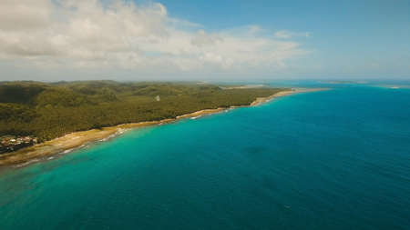 Aerial view: sea and the tropical island with rocks, beach and waves. Coastline of the tropical island Siargao with the mountains and the rainforest on a background of ocean with big waves. Seascape: sky, clouds, ocean. Philippines. Travel concept.の写真素材