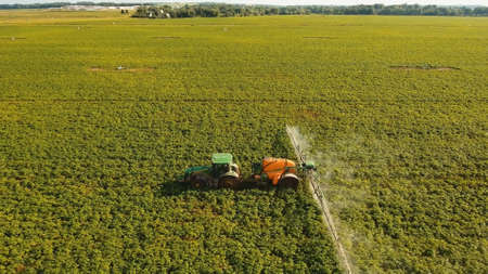 Aerial view tractor spraying the chemicals on the large green field. Spraying the herbicides on the...