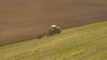Farm tractor plowing a green field, a lot of birds flying around him.Aerial view:tractor plowing the...