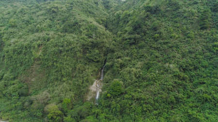 Aerial view of waterfall in the mountains of Filipino cordillera. Waterfall in the mountains. Waterfall flowing on the slopes of mountains covered with tropical vegetation. Philippines, Luzonの写真素材