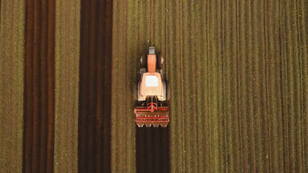 Farmer in tractor preparing land with seedbed cultivator in farmlands. Tractor plows a field. Agricultural work in processing, cultivation of land. Farmers preparing land and fertilizing. Agricultural workers with tractors.の写真素材