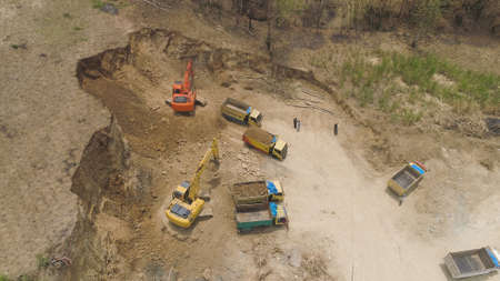 excavator at construction site cuts hill and loads truck with earth. aerial view Heavy machinery...
