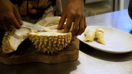 hand peeling and cuts durian fruit. caucasian man peeling durian in kitchen roomの写真素材