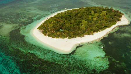 Tropical island and sandy beach surrounded by atoll and coral reef with turquoise water, aerial...