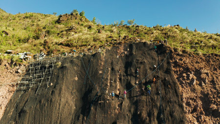 Protection of road from mountain slough, rockfall with metal accumulative restraining net fences. Workers constructing anti-landslide concrete wall prevent protect against rock slides. Rockfall protection. Workers strengthen the slope of the mountain with steel grid preventing rockfall and landslide on the road.の写真素材