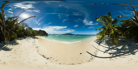 A serene beach lined with swaying palm trees offers cool shade, while gentle waves lap at the pristine shoreline. La Digue, Seychelles. 360 panorama VR.の写真素材