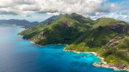 Turquoise waters stretching along the green mountain slopes with clear skies above. Seychelles,...