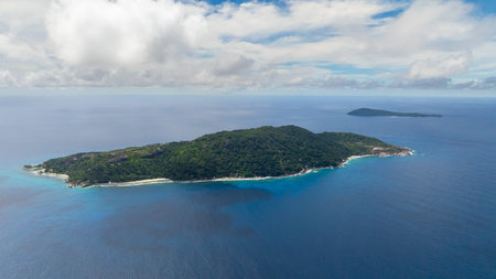 A distant island surrounded by deep blue ocean and greenery under a cloudy sky. Felicite, Seychelles.の写真素材