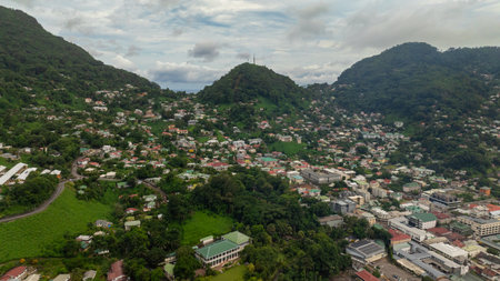Dense residential area nestled between green hills with lush vegetation, various buildings, and winding roads visible. Seychelles, Mahe.の写真素材