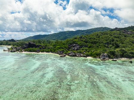 Aerial shot of lush green hills meeting the coast with cloudy skies overhead. La Digue, Seychelles.の写真素材