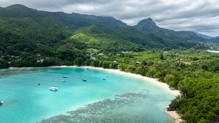 A green hillside overlooks a tranquil turquoise bay, with boats dotting the clear water. Seychelles, Mahe.の写真素材