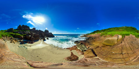 A dramatic coastline featuring red rock formations and a sandy beach, with waves crashing against...