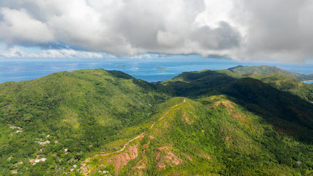 Lush, green hills cascade towards the ocean under a sky of drifting clouds, with small islands on the horizon. Praslin, Seychelles.の写真素材