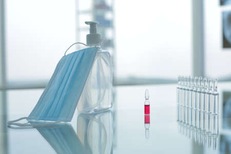 Vial with red and transparent vaccines medical protective mask and antiseptic on glass table