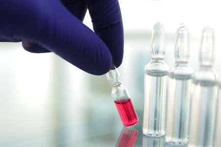 Doctor in rubber blue gloves picks up a bottle of vaccine with his fingers in hospitalの写真素材