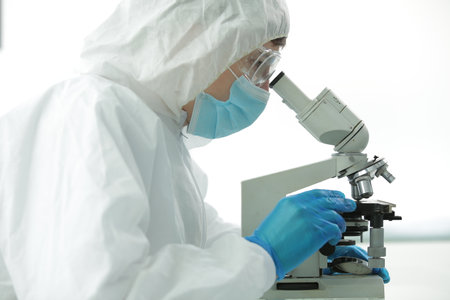 Doctor in a protective suit wearing a mask wearing blue gloves in a laboratory looks through a...