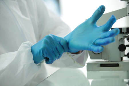 Doctor in protective suit goggles straightens blue gloves near microscope in medical laboratory in hospitalの写真素材