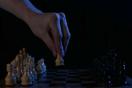 Human hand takes a wooden chess pawn on a black background