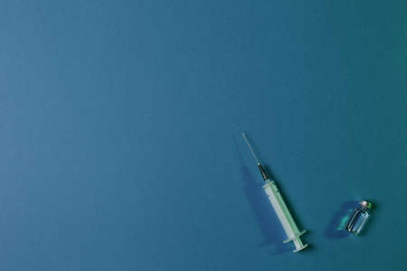 Medical syringe and vial with vaccine on blue background