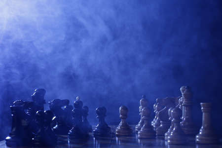 Chess is a board game. Chess wooden pieces on a dark background in smokeの写真素材