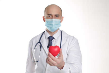 Doctor in Protective Mask with stethoscope in protective mask writing pad and red heart in clinic on...