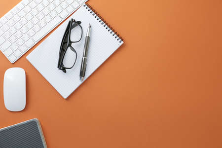 Glasses white keyboard and mouse pen notepad and diary on orange background