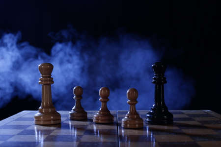 Wooden chess is a board game. Chess pieces on a dark background in smoke
