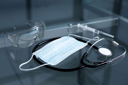 Protective medical mask stethoscope gauze mask syringe and vial with vaccine on a glass tableの写真素材