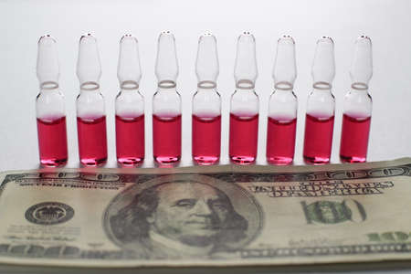 Glass vials with vaccine red and US dollars on a white background