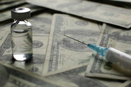 Vial with medical syringe vaccine and many dollarsの写真素材