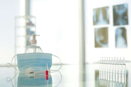 Vials with vaccine syringe protective medical mask and antiseptic on a glass tableの写真素材