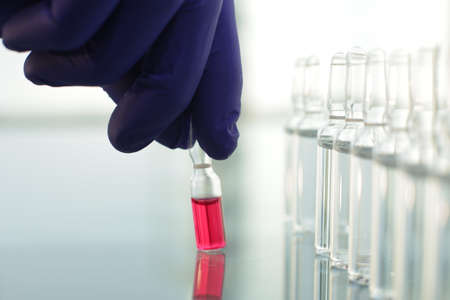 Doctor in rubber blue gloves picks up a bottle of vaccine with his fingersの写真素材